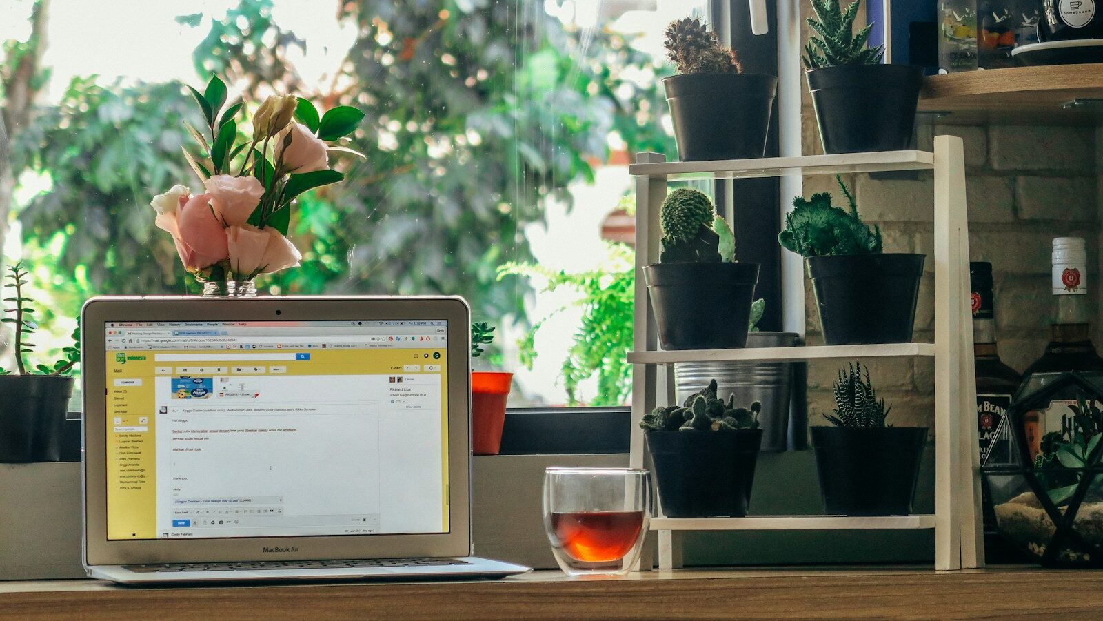 Workplace well-being. Image description: a laptop turned on beside clear rocks glass with liquor on brown table